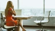 Woman in dress looks outside of window whilst taking call.