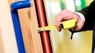 A Checkmate Fire door installer using a tape measure to check the width of a fire door.