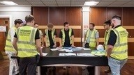 Members of the Checkmate Fire team stood around a table discussing a project.