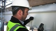 A Checkmate Fire inspector using a handheld device to carry out inspection work on a wall.